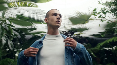 a man in a white t - shirt and blue jean jacket standing in front of