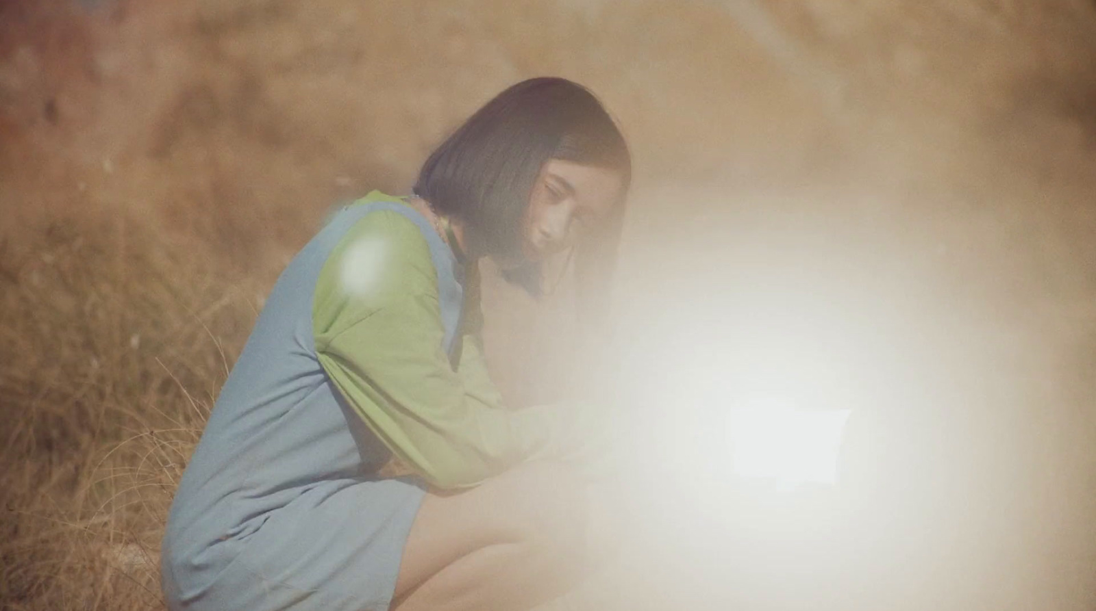 a woman sitting in a field with a light shining on her