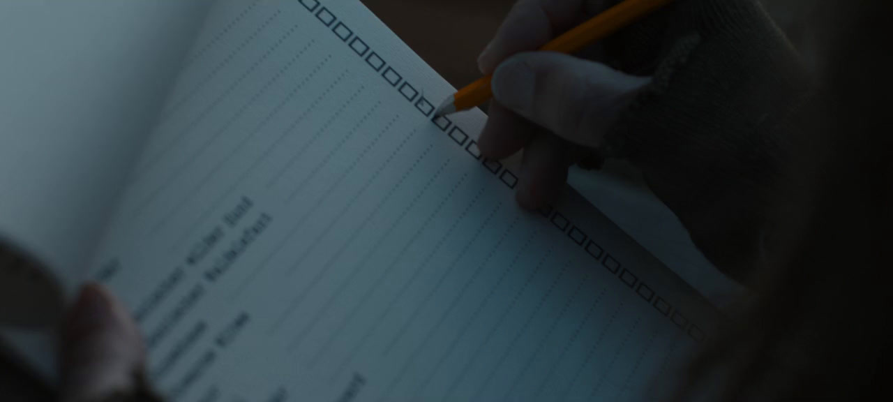 a person writing on a notebook with a pencil