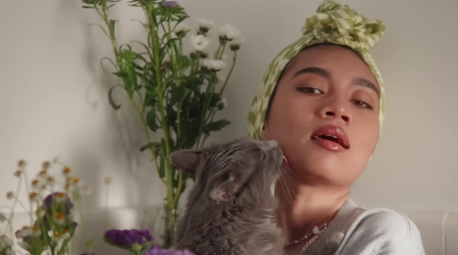 a woman holding a cat next to a bunch of flowers