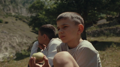 a young boy holding an apple while sitting on the ground