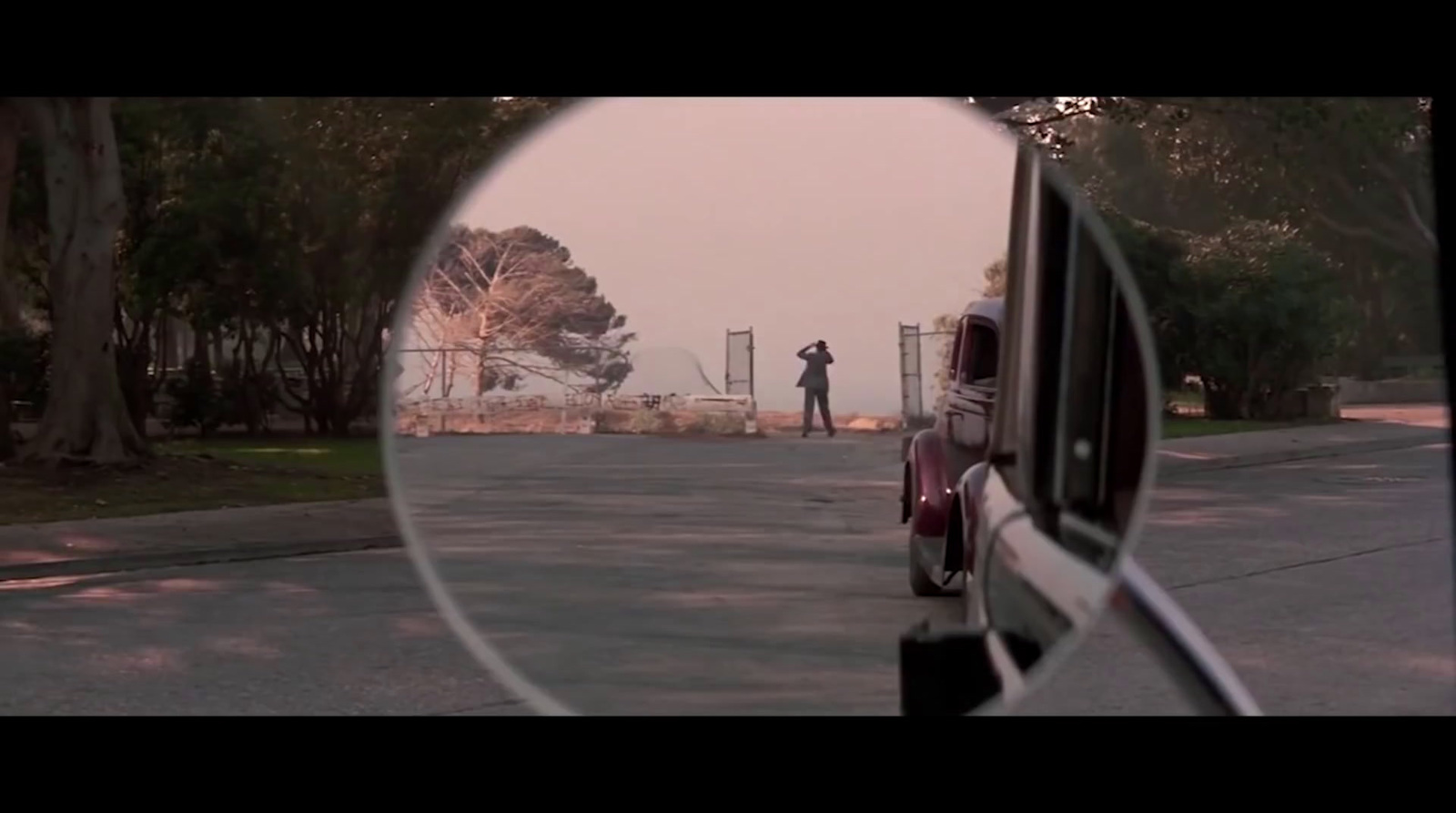 a rear view mirror reflecting a man standing on a street