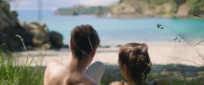 a man and a woman sitting on the grass looking at the water