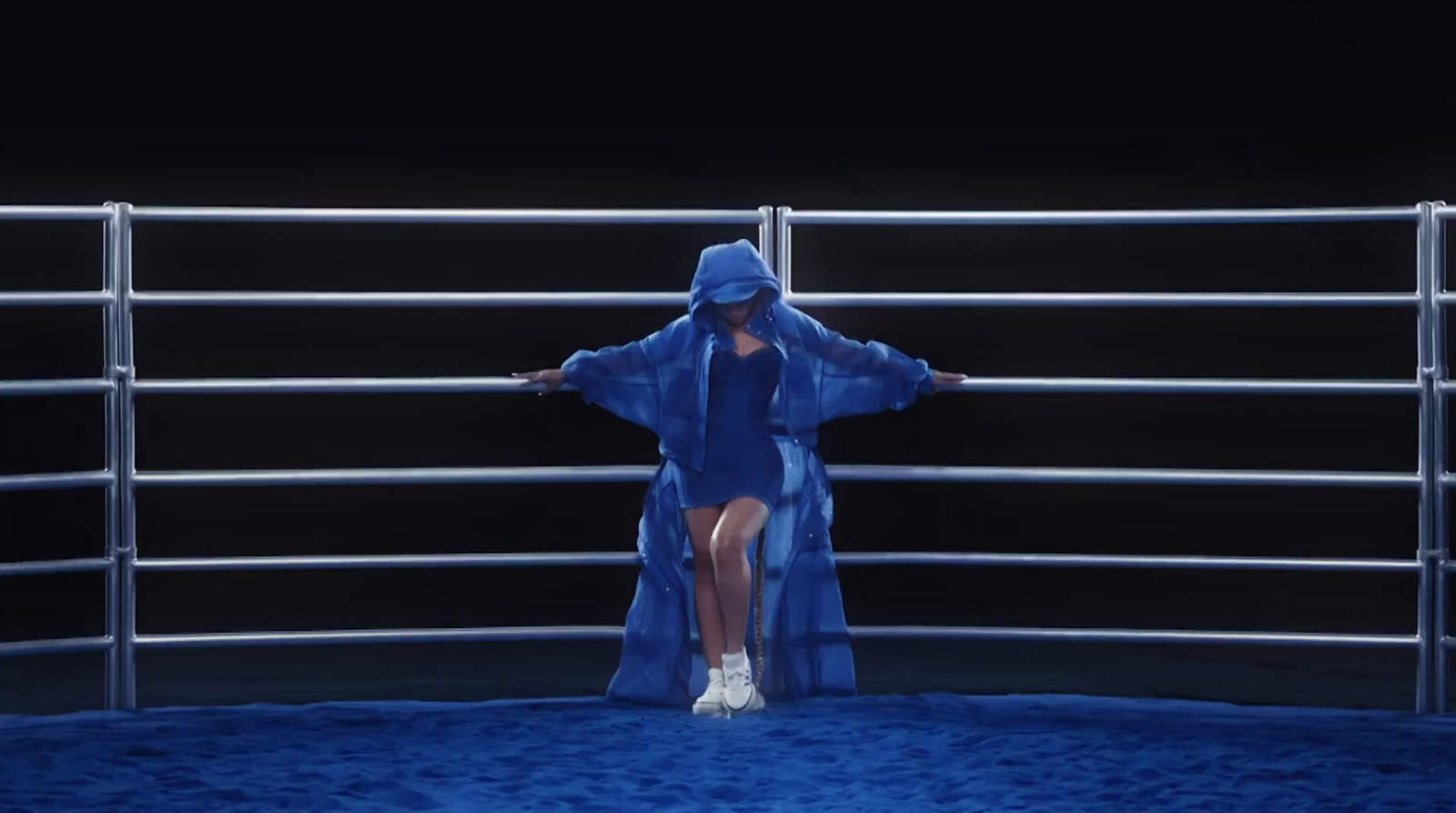 a woman in a blue robe standing in front of a metal fence