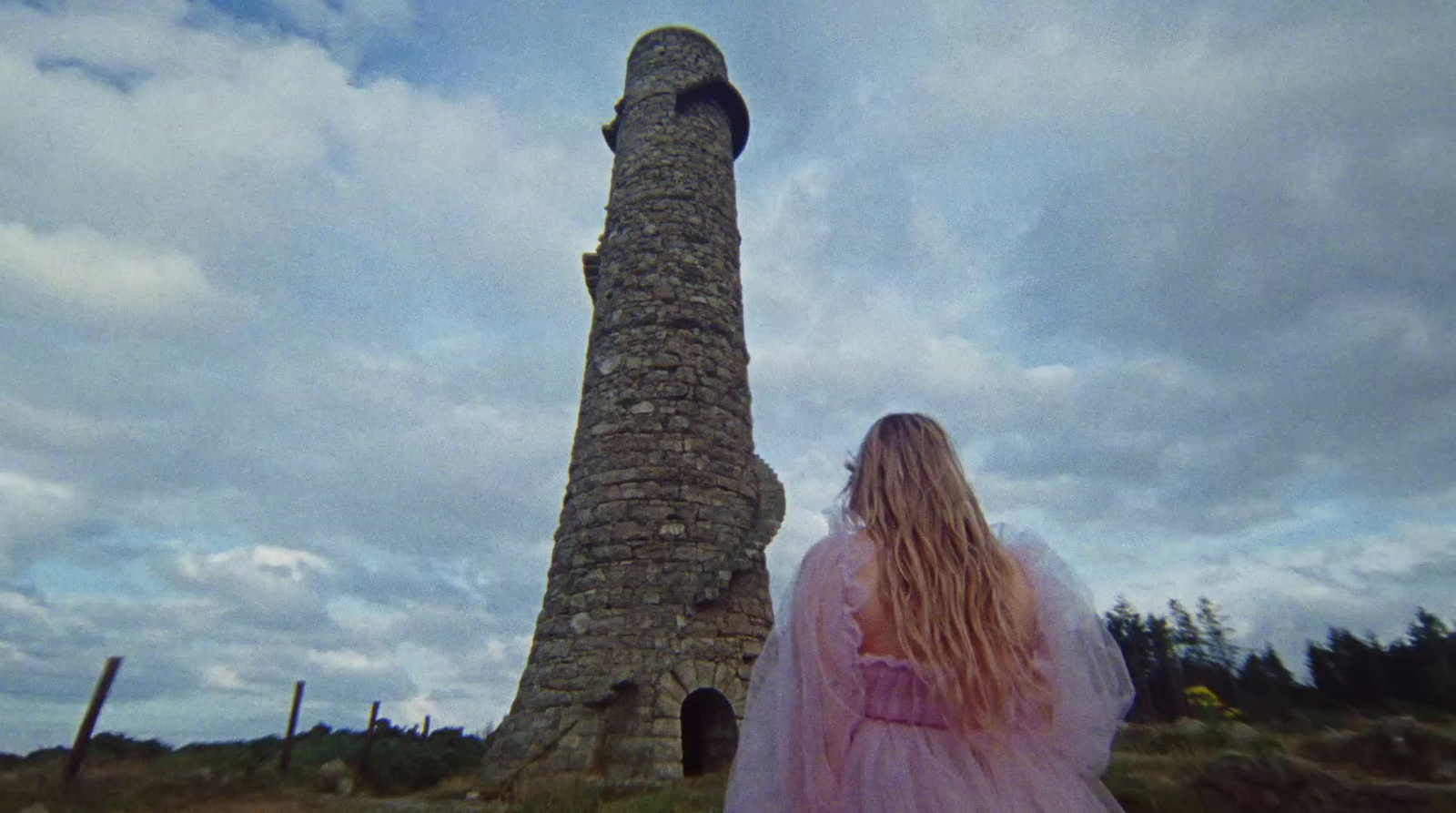 a woman in a pink dress standing next to a stone tower