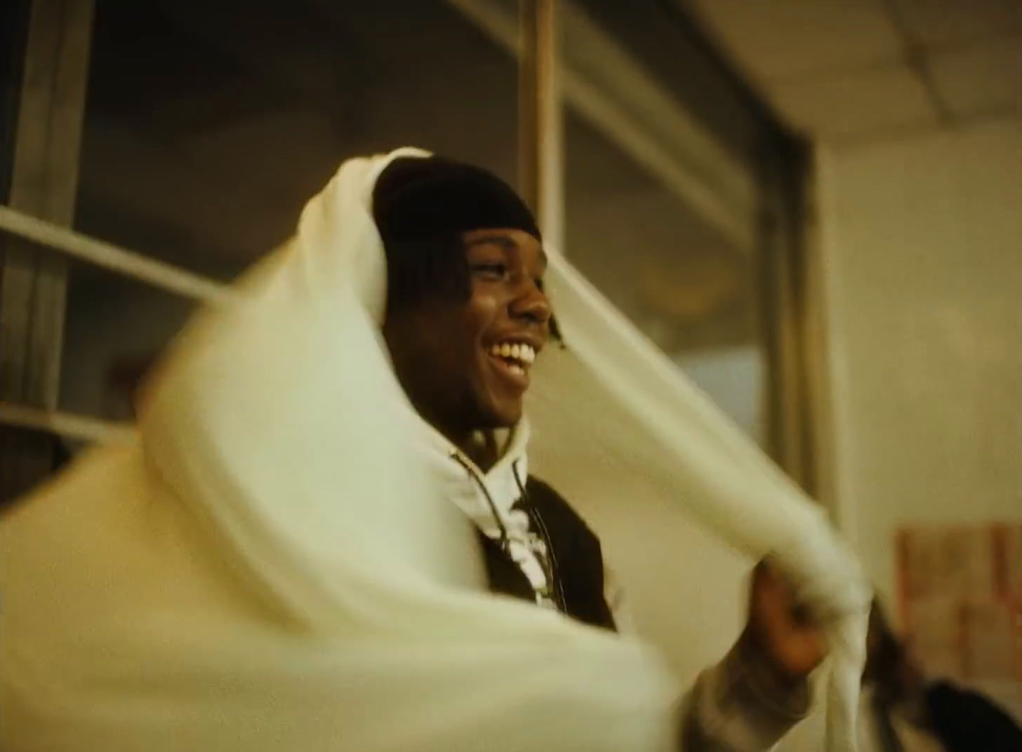 a smiling man wrapped in a blanket in front of a window