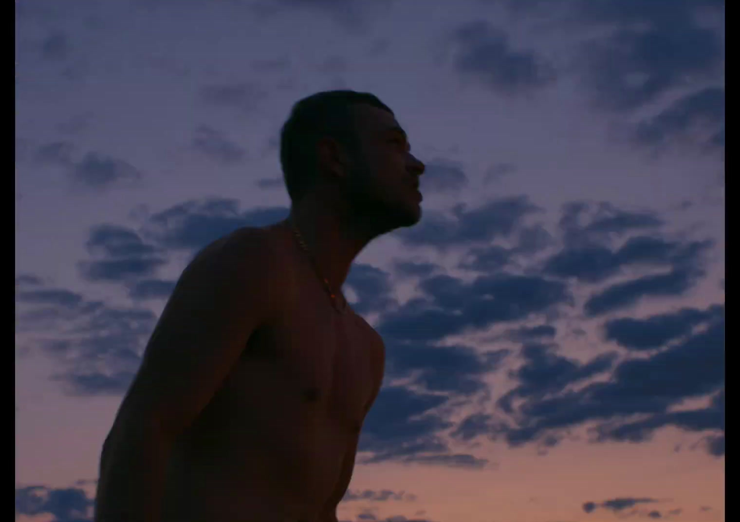 a man without a shirt standing in front of a cloudy sky