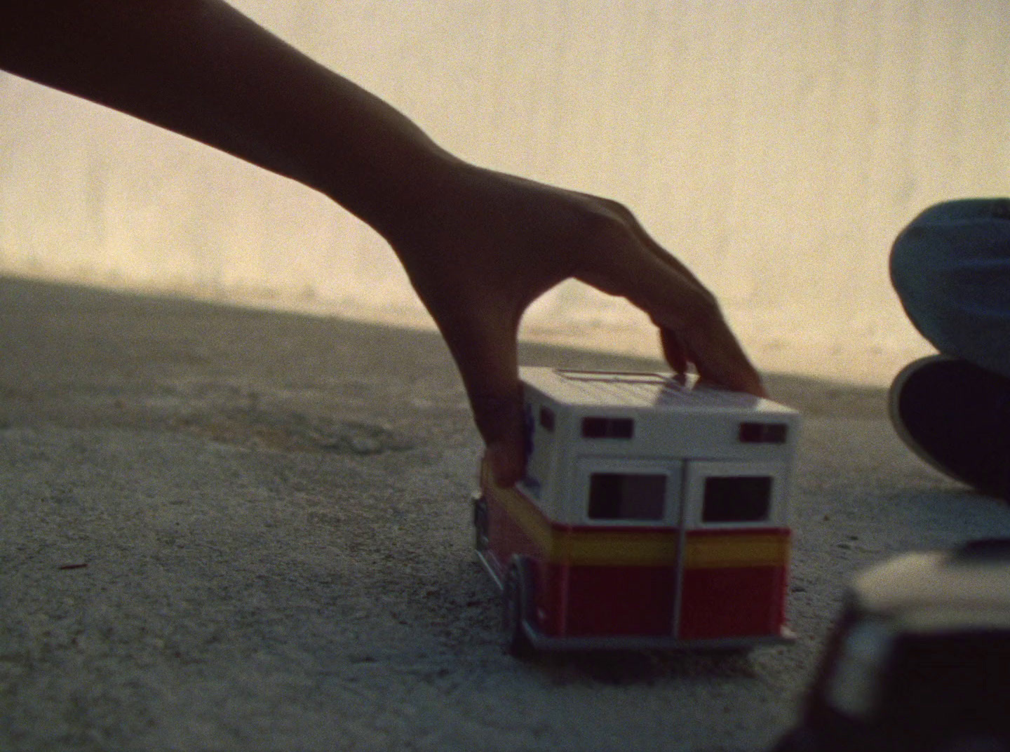 a hand reaching for a toy bus on the ground