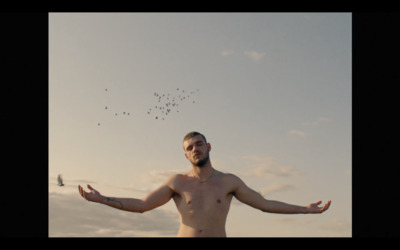 a shirtless man with his arms spread out in front of a flock of birds