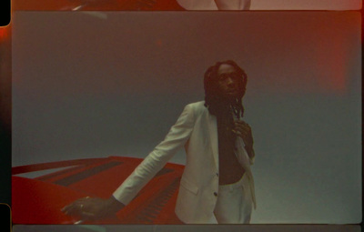 a man with dreadlocks standing in front of a red car