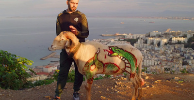 a man standing on top of a hill next to a goat