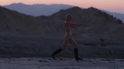 a naked man walking in the desert at sunset