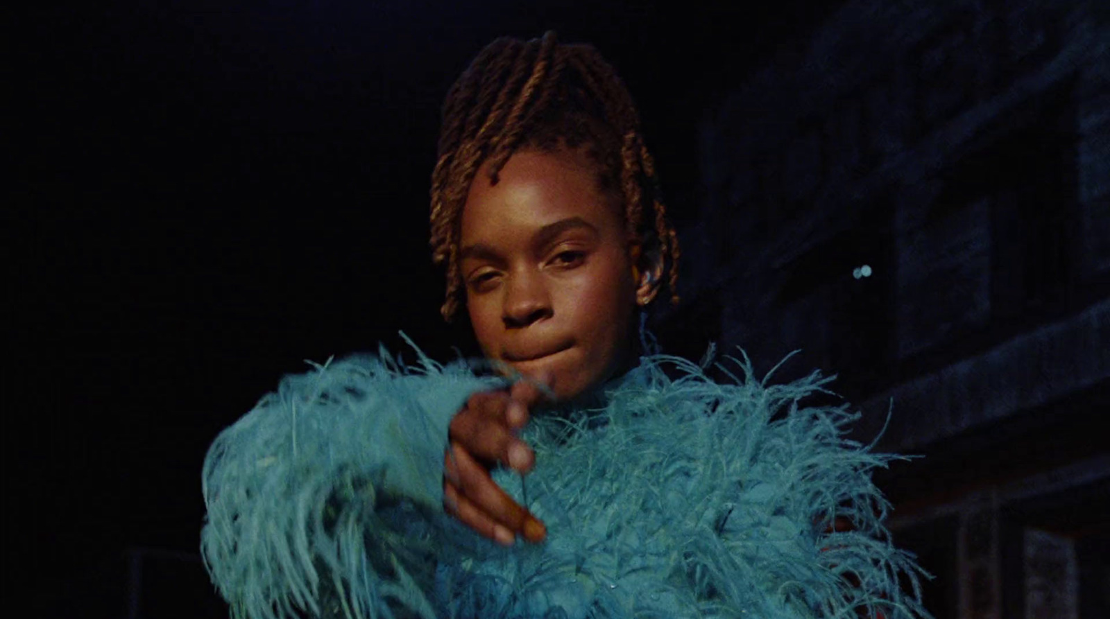 a woman in a blue feather coat pointing at the camera