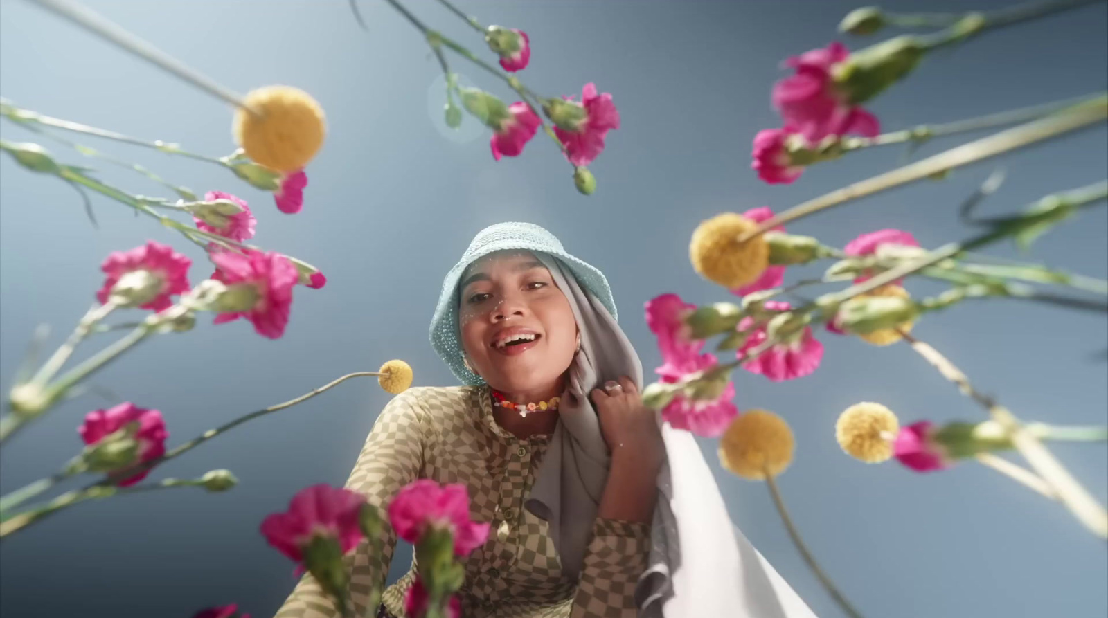 a woman wearing a blue hat and scarf standing in a field of flowers