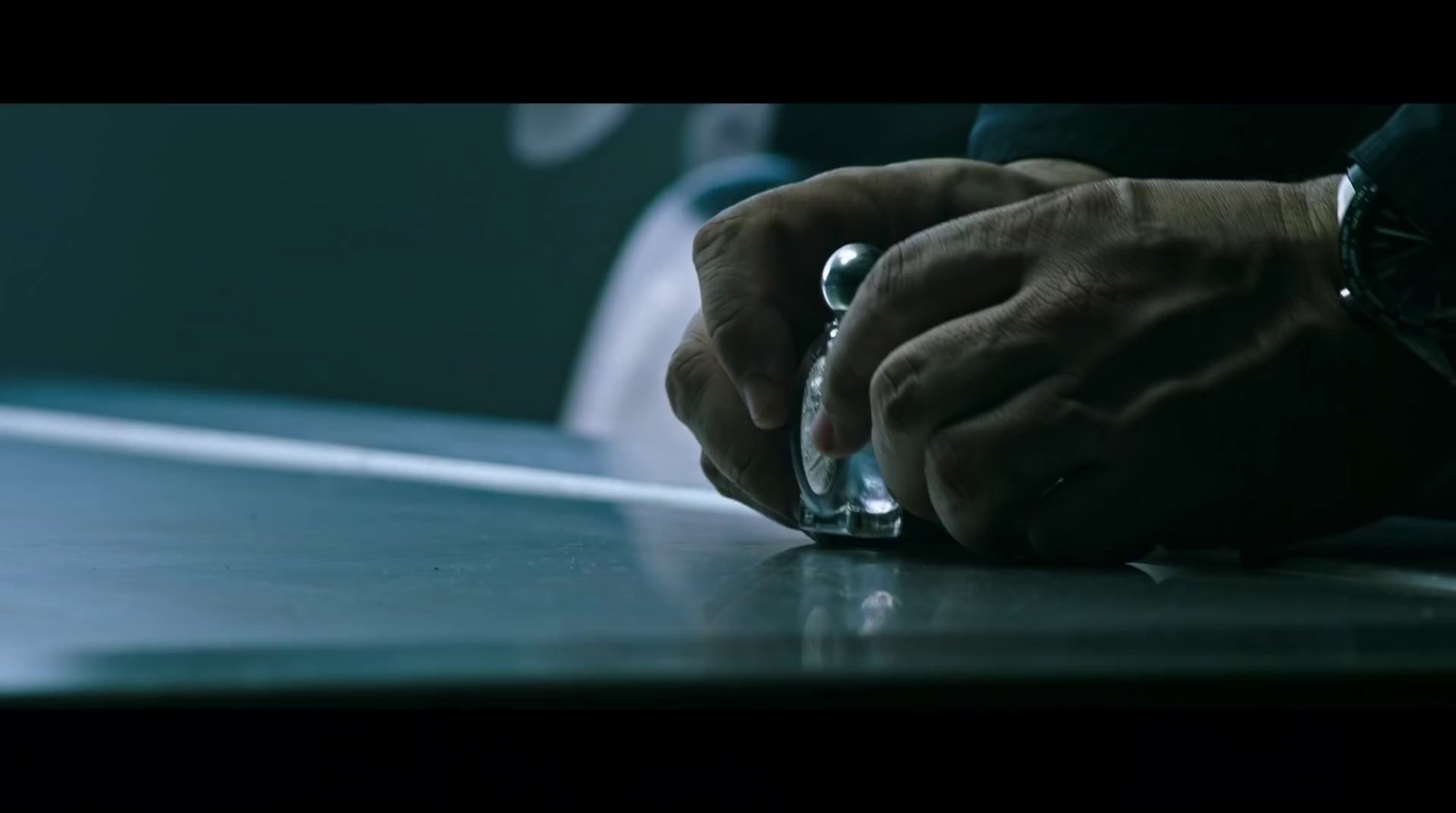 a man's hand on top of a glass on a table