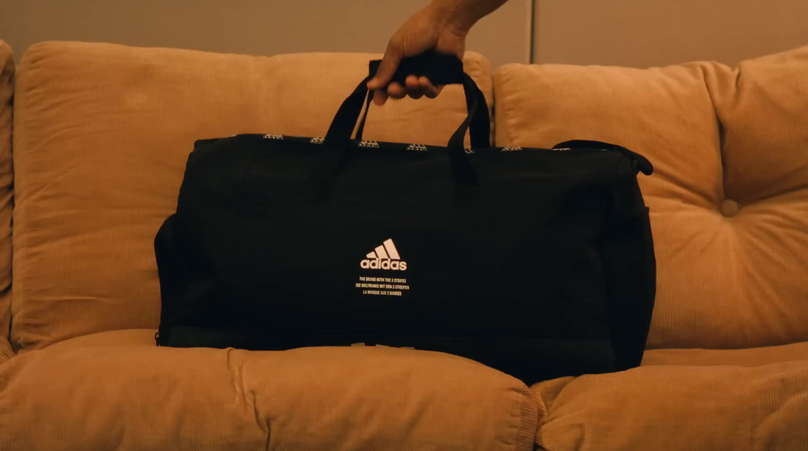 a person holding a black adidas bag on a couch