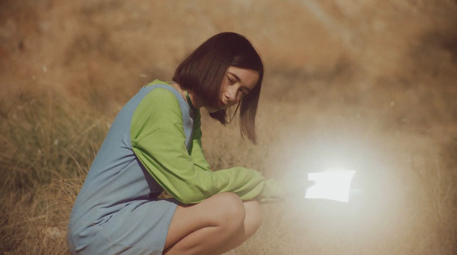 a woman kneeling down in a field with a light