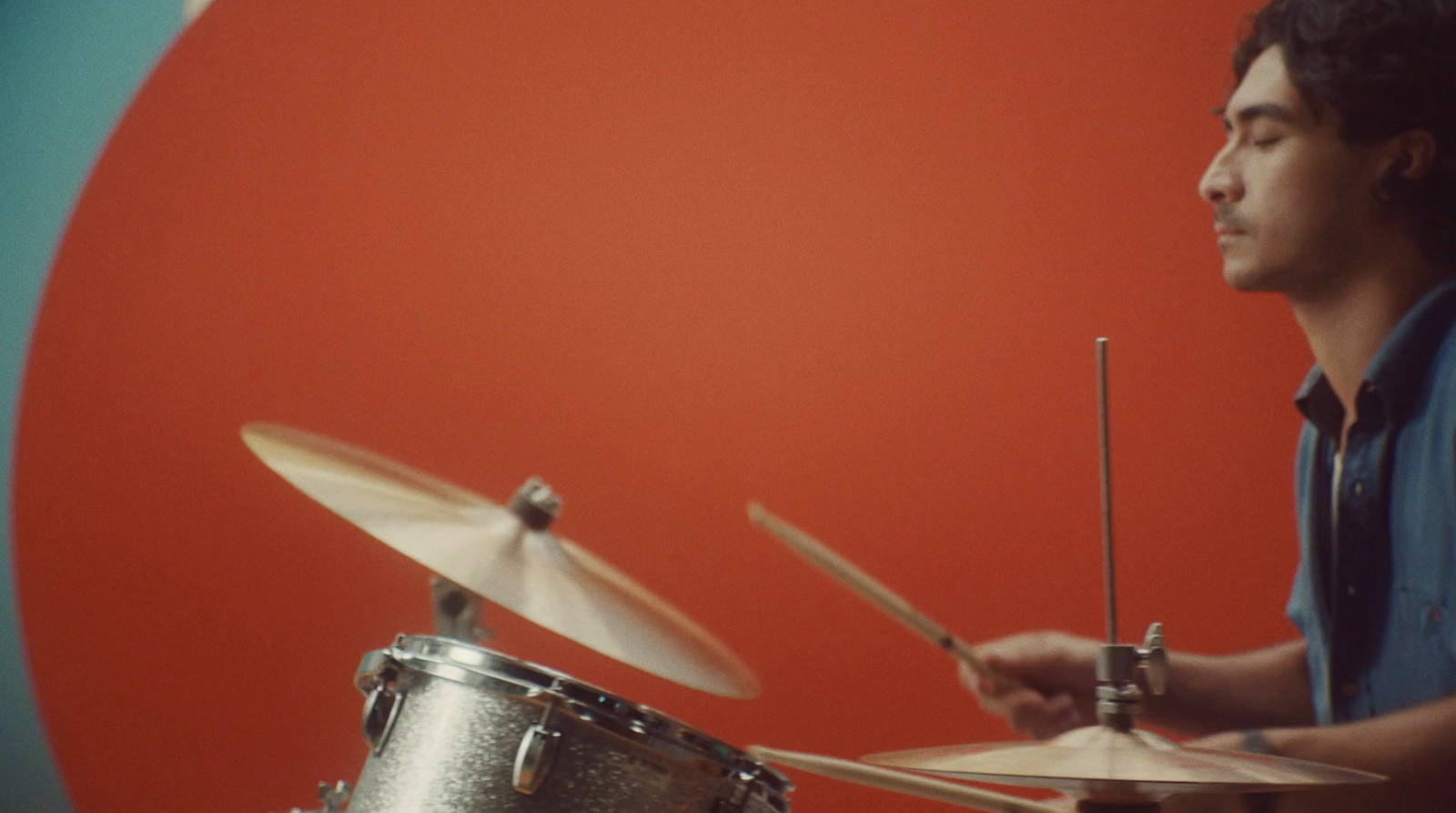 a man playing drums in front of a red and blue background