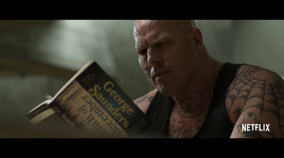 a bald man reading a book while wearing a black tank top