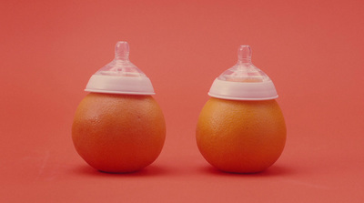 two oranges with a baby bottle on top of them