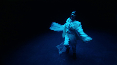 a woman in a white suit is dancing in the dark