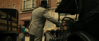 a man in a suit and hat standing next to a truck