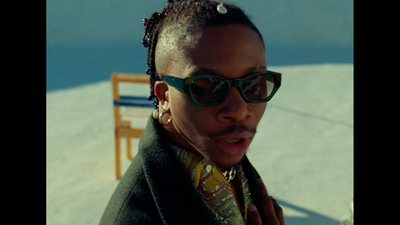 a man wearing sunglasses and a tie standing in front of a chair