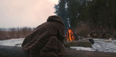 a person sitting in front of a fire in the woods