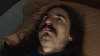 a man with long hair and a moustache laying on a bed