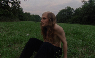 a man with long hair sitting on the ground