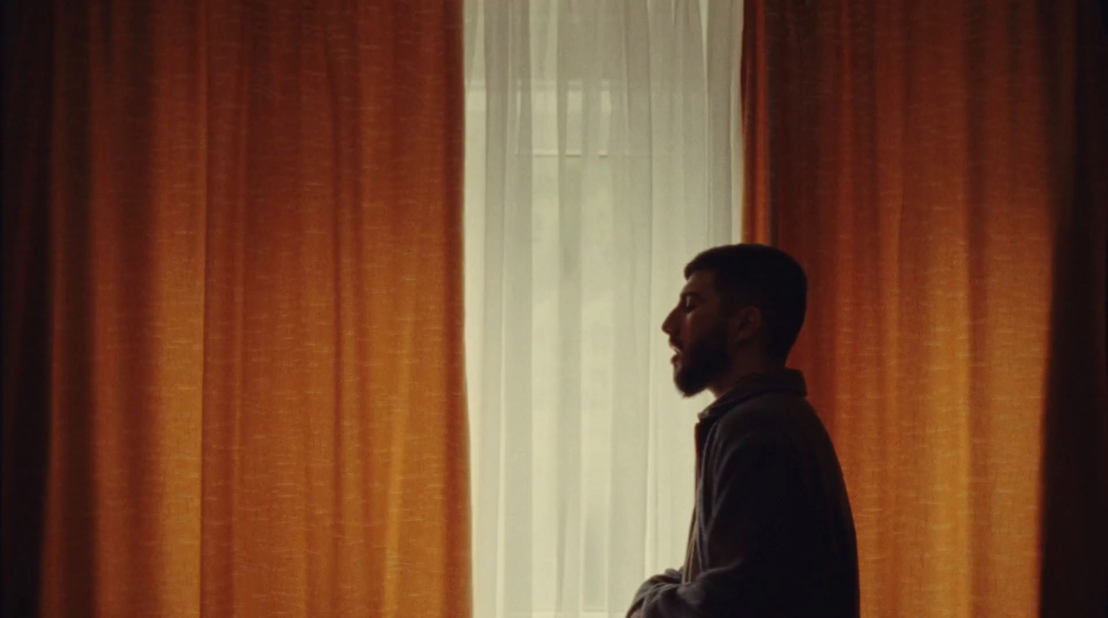 a man standing in front of a window with orange curtains