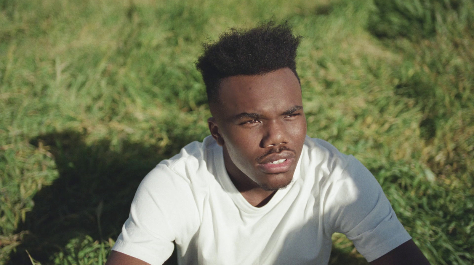 a man sitting in the grass wearing a white shirt