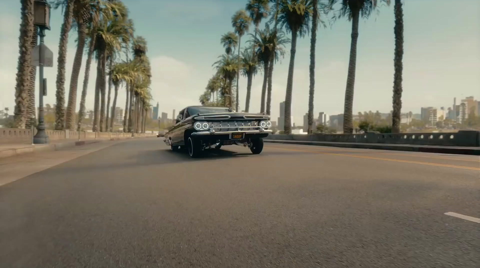 a black car driving down a street next to palm trees