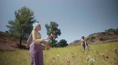 two people in a field with flowers and trees in the background