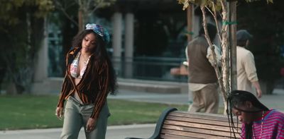 a woman standing next to a man sitting on a bench