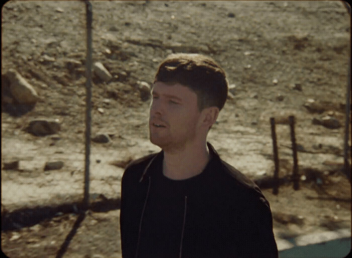 a man in a black shirt standing in a dirt field