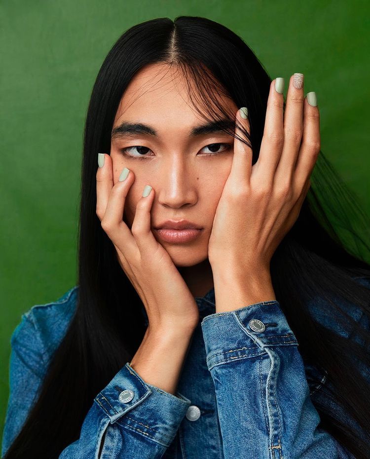 a woman with long black hair holding her hands to her face