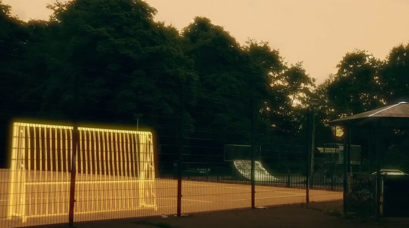 a tennis court with a yellow fence and trees in the background