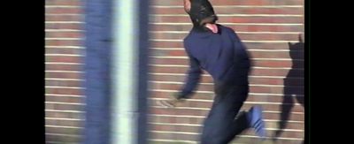 a man in a black suit is walking by a brick wall