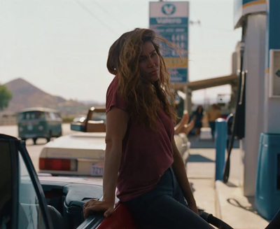 a woman sitting on the hood of a car at a gas station