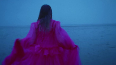 a woman in a pink dress walking on the beach