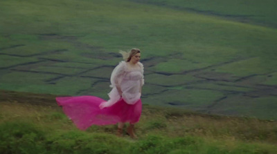 a woman in a pink dress is walking on a hill