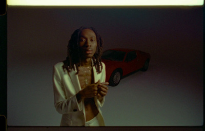 a man with dreadlocks standing in front of a car