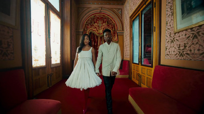 a man and a woman dressed in white walking down a red carpeted hallway