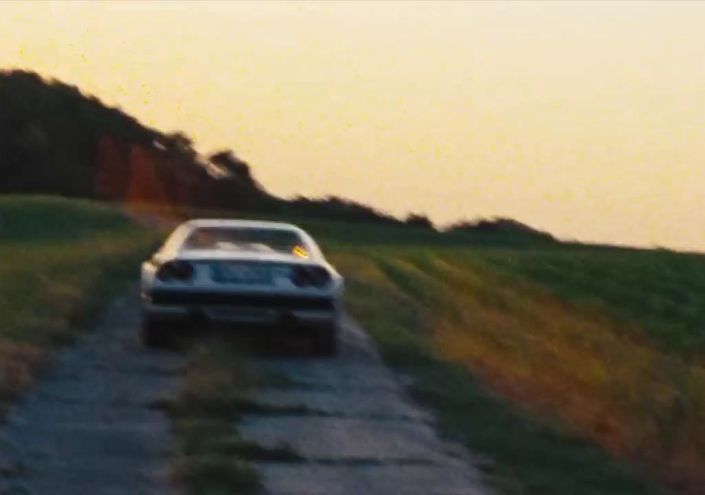 a car driving down a dirt road next to a lush green field