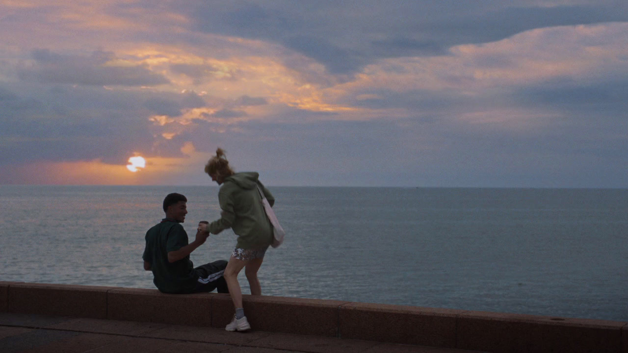 a man and a woman sitting on a wall next to the ocean