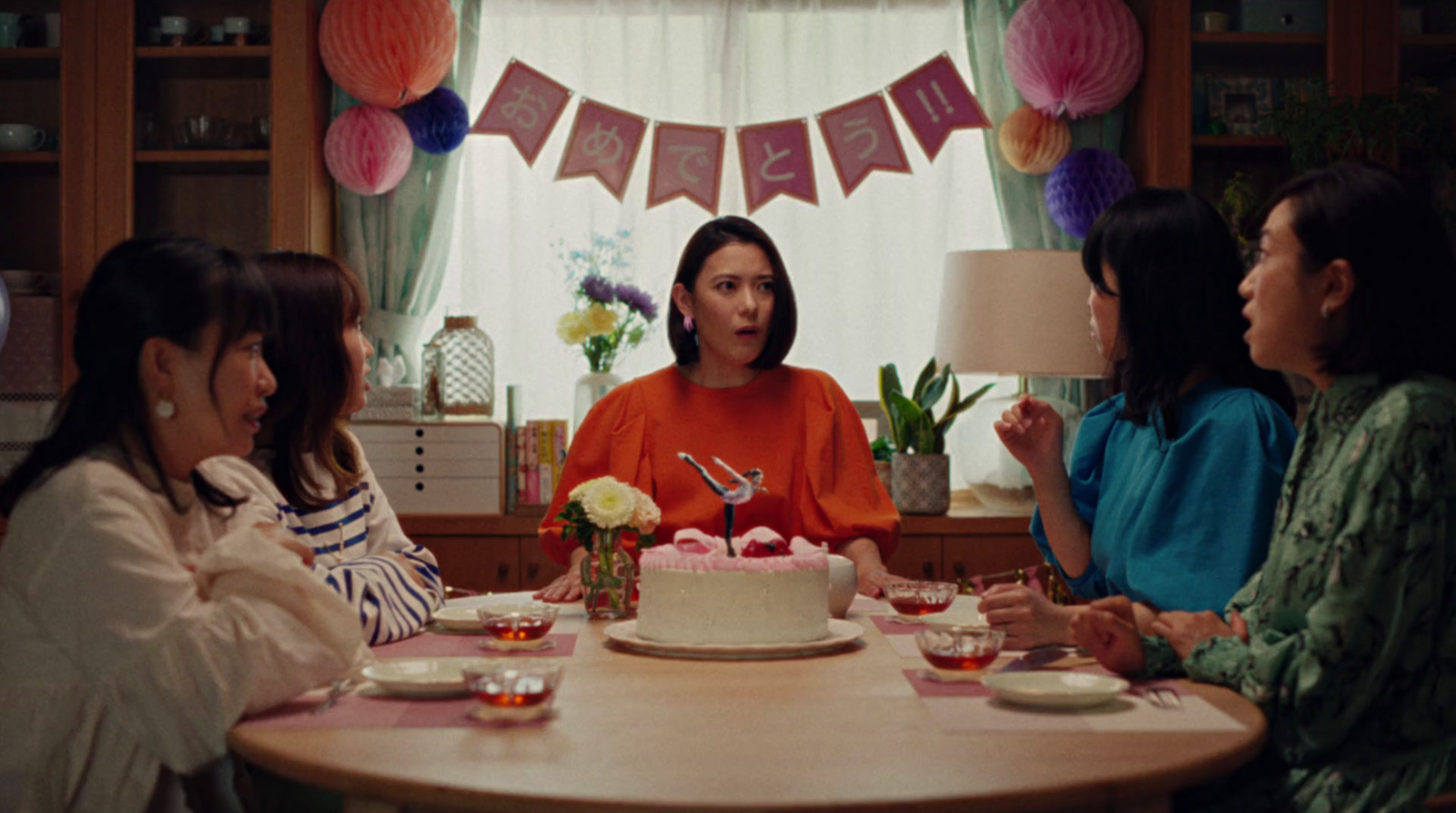 a group of women sitting around a table with a cake