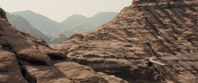 a bird flying over a rocky landscape with mountains in the background