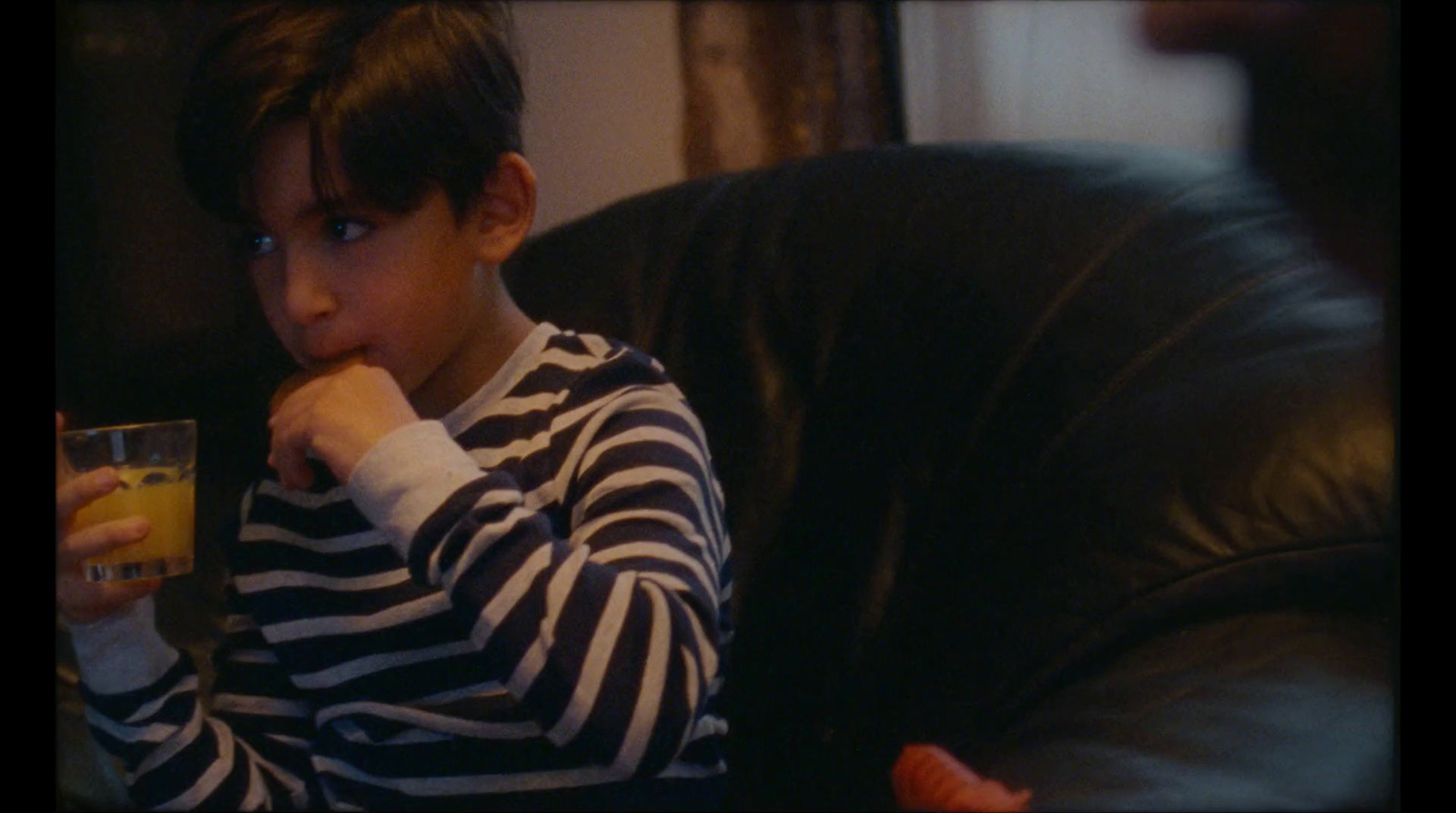 a young boy sitting on a couch holding a glass of orange juice