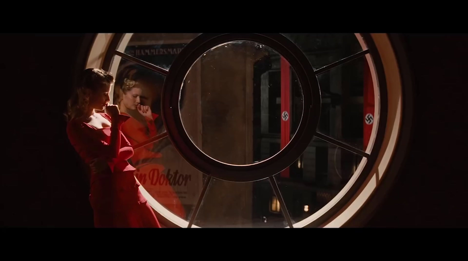 a woman in a red dress standing in front of a round window